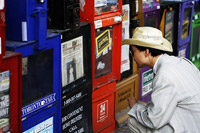 Man squatting to read newspaper headlines