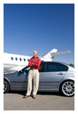 A man standing in front of a luxury car and a private plane